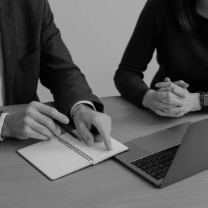 Dos figuras humanas en blanco y negro, una guiando a la otra hacia una zona más iluminada, simbolizando el acompañamiento y crecimiento personal que define el proceso de mentoría.